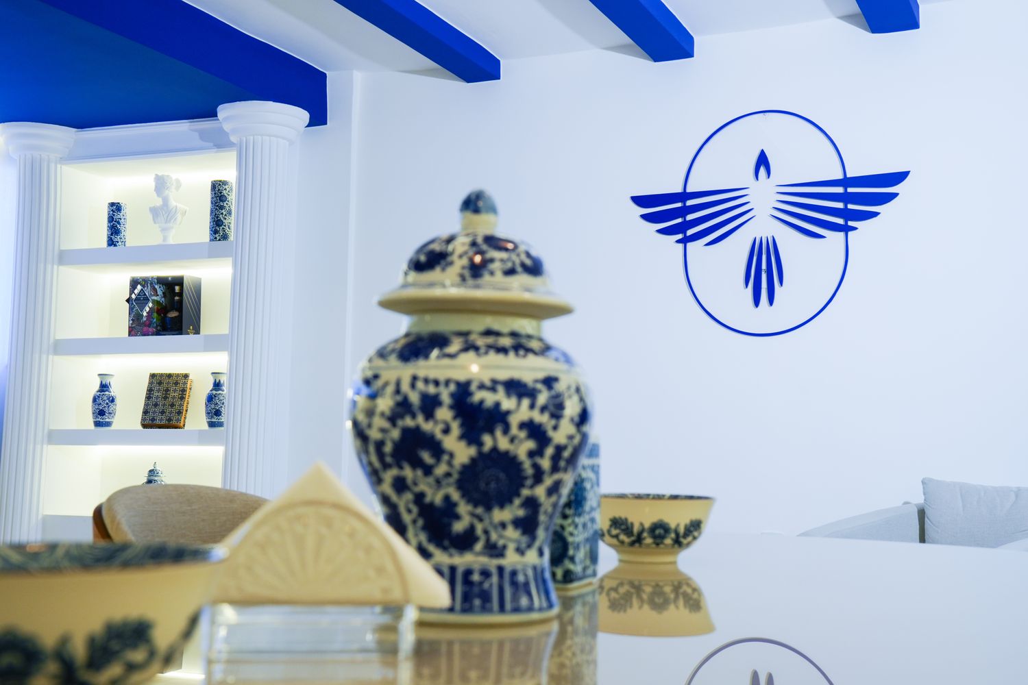 Estante com peças em porcelana azul e branca e o símbolo da marca na parede